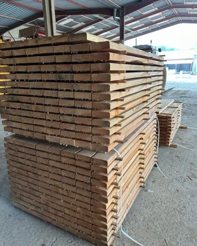 Empilement de planches de bois sous un toit en métal dans une scierie.